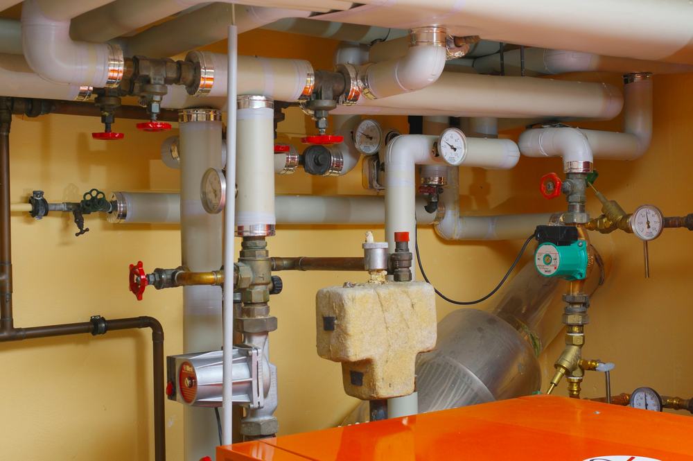 Insulated heating pipes, valves and gauges above an orange boiler in a utility room