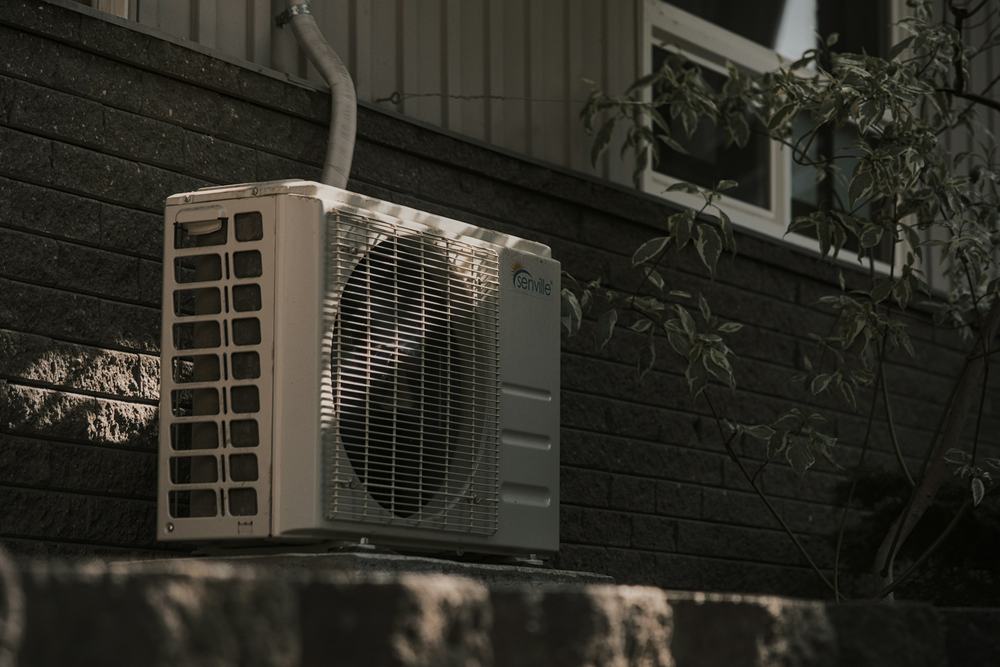 Outdoor air conditioning condenser mounted against a dark brick wall