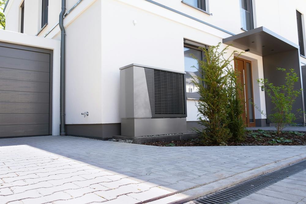 Outdoor heat pump unit beside a modern white house and paved driveway