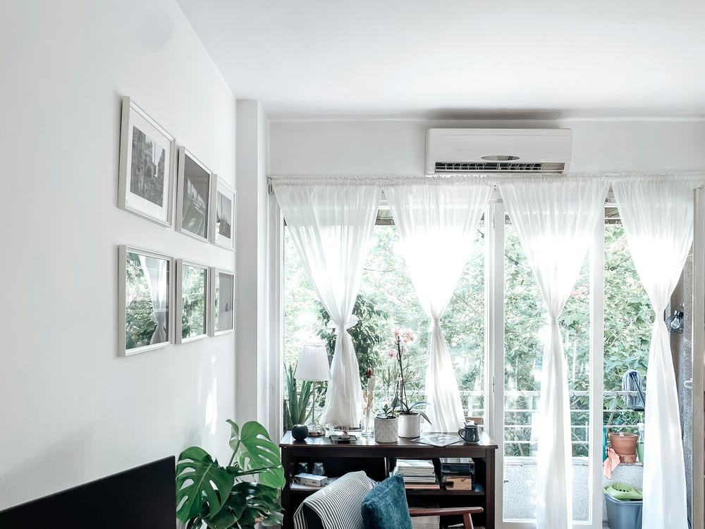 Bright living room with a white ductless mini-split unit mounted above sheer-curtained windows