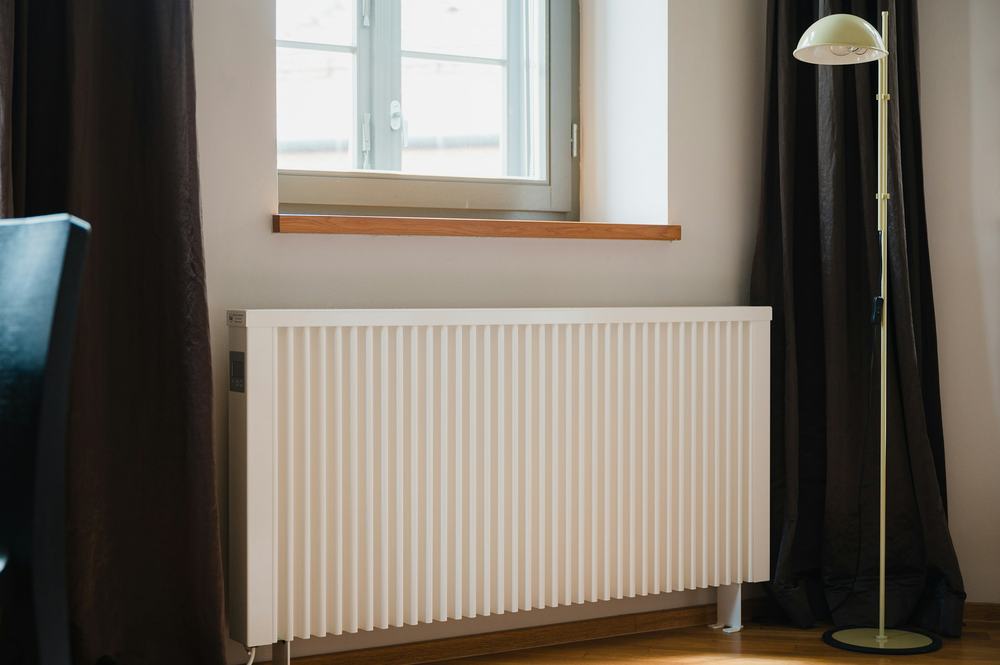 White panel radiator beneath a window between dark curtains