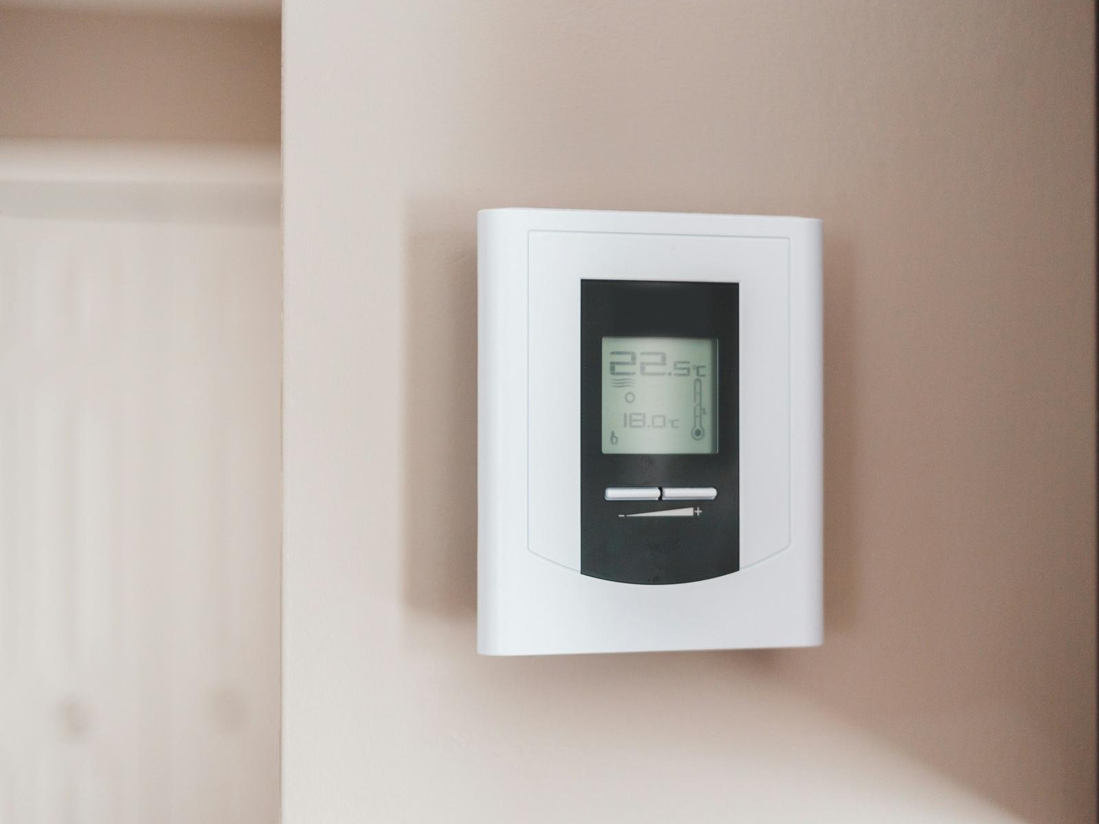 White digital wall thermostat on a soft beige wall