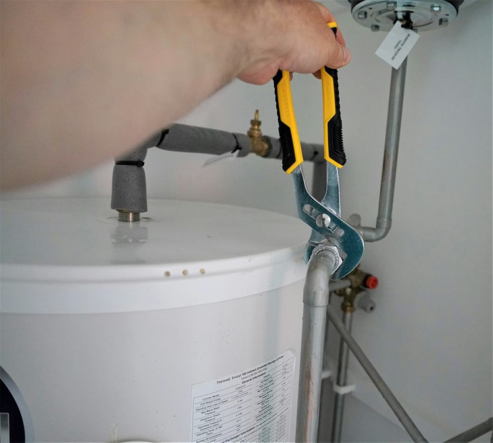 Hand tightening a pipe fitting above a white water tank with an adjustable wrench